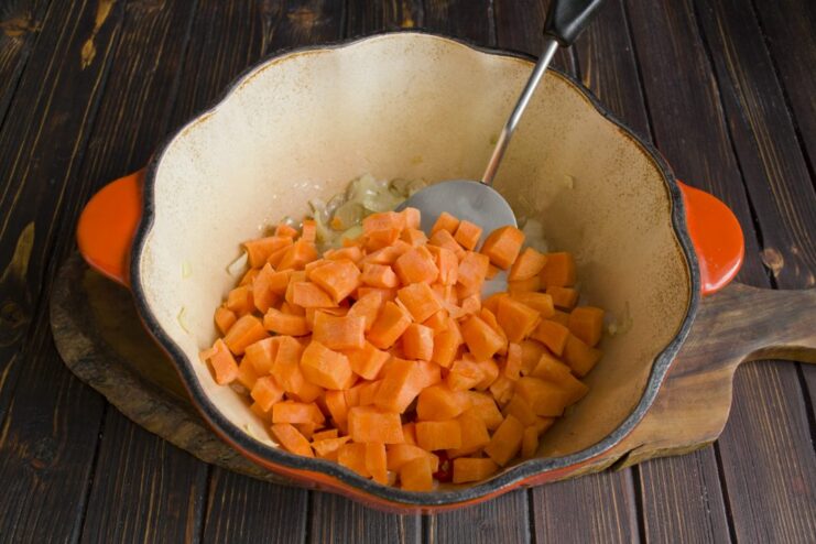 Adding diced carrots to the onions and chili for extra sweetness and color. Diced carrots being added to the sautéed onions in the pot.