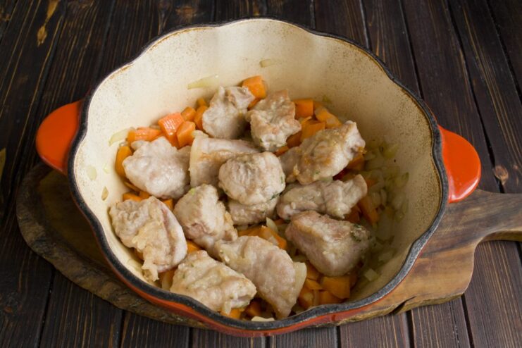 Layering the seared pork over the sautéed vegetables. Seared pork pieces being placed on top of the cooked vegetables in the pot.