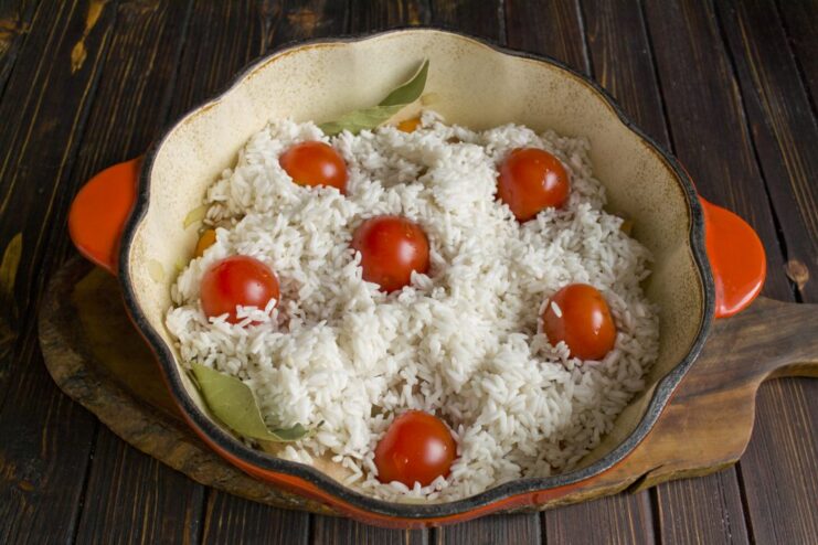 Tucking cherry tomatoes into the rice for a burst of juicy flavor. Whole cherry tomatoes being placed on top of the rice layer in the pot.