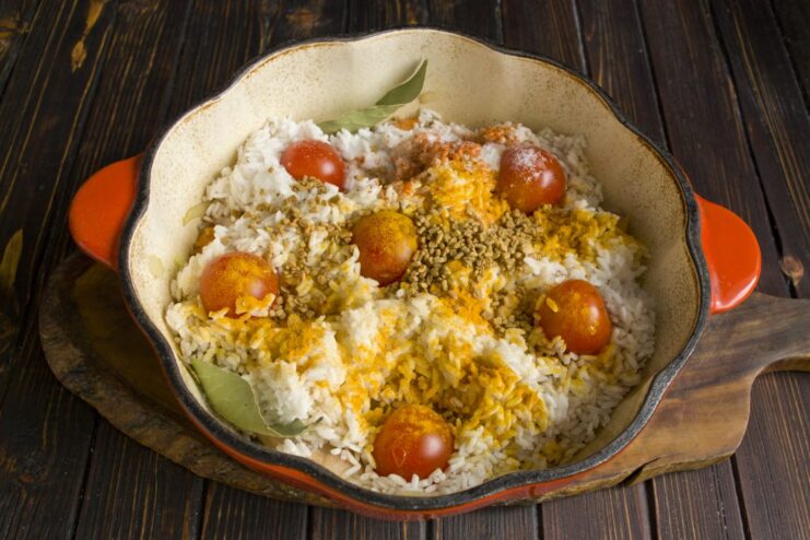 Sprinkling spices like turmeric and paprika over the rice for flavor and color. A mix of colorful spices being sprinkled over the rice in the pot.