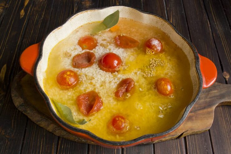 Pouring in water and adding dried apricots to the plov. Water being poured into the pot, with dried apricots scattered on top of the rice.