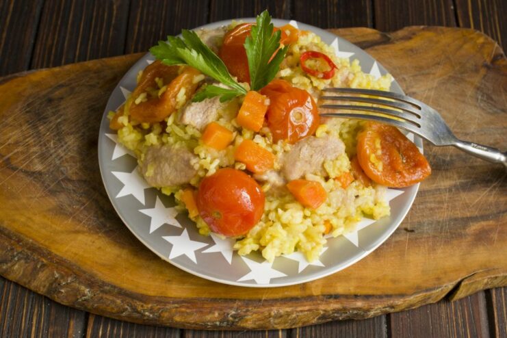 The finished Pork Plov, fluffy and aromatic, ready to be served. The cooked Pork Plov with apricots and tomatoes in a dutch oven, ready to serve.