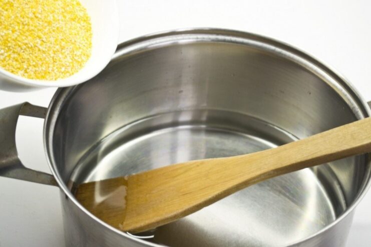Cooking Polenta: Pouring Corn Grits into Boiling Water Corn grits being poured from a container into a pot of boiling water.