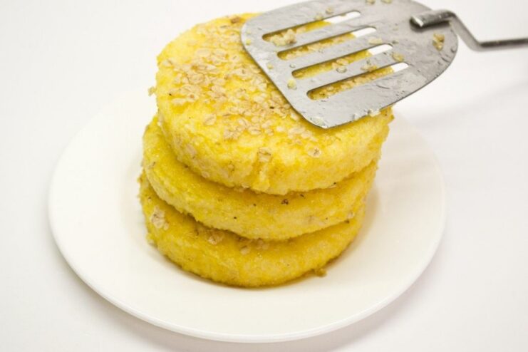 Frying Polenta Cakes Until Golden Brown and Crispy Oat-crusted polenta cakes frying in a pan with hot oil until golden.