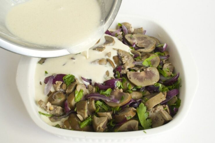 Assembling the Kidney Pudding Before Baking Liquid batter being poured over a layer of cooked kidneys and onions in a baking dish.