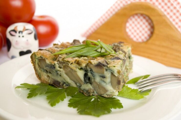 A slice of savory kidney pudding in a white baking dish, showing the fluffy batter and kidney filling.