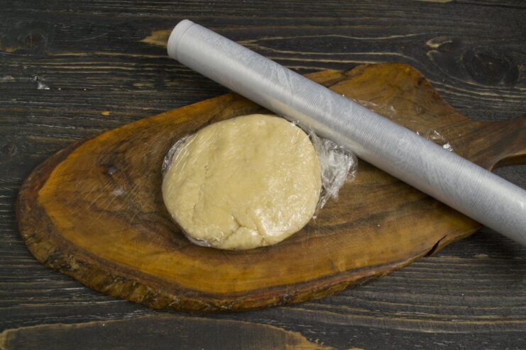 Resting the Ravioli Dough is a Crucial Step for Elasticity A smooth ball of ravioli dough being wrapped in clear plastic wrap to rest.