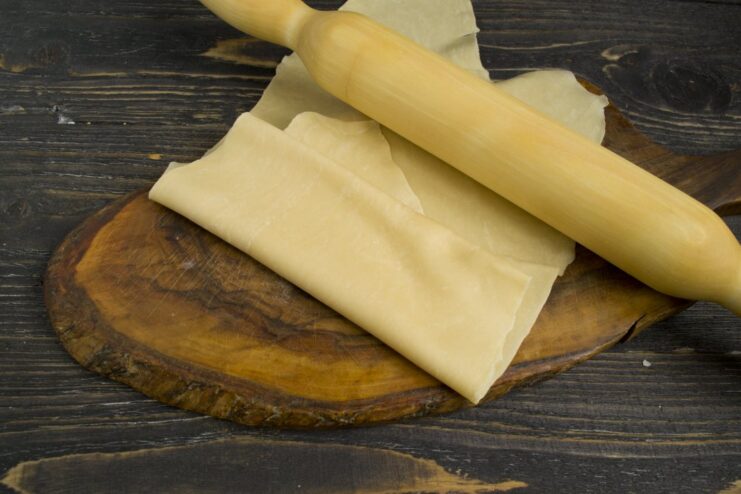 How to Roll Ravioli Dough Thinly by Hand A person using a rolling pin to roll out a large, thin sheet of pasta dough.