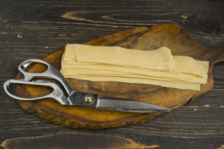 Preparing Dough Strips for Assembling Ravioli A sheet of thinly rolled pasta dough being cut into long, even strips with a knife.