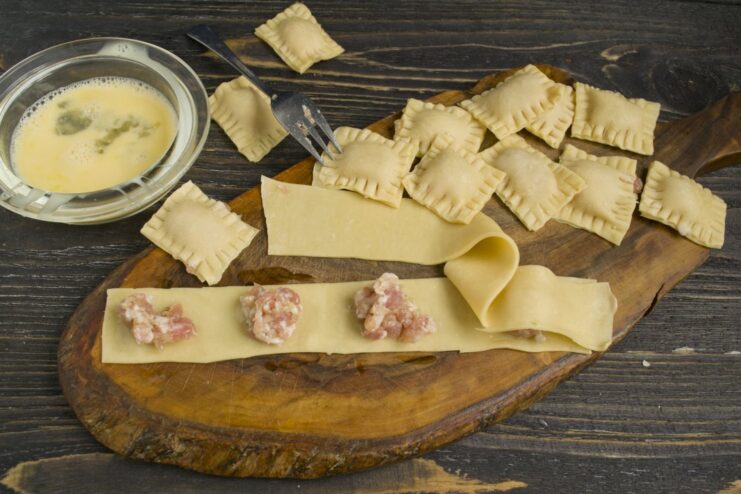 Step-by-Step Guide to Assembling and Sealing Ravioli Uncooked square ravioli being formed, with filling inside and edges crimped with a fork.