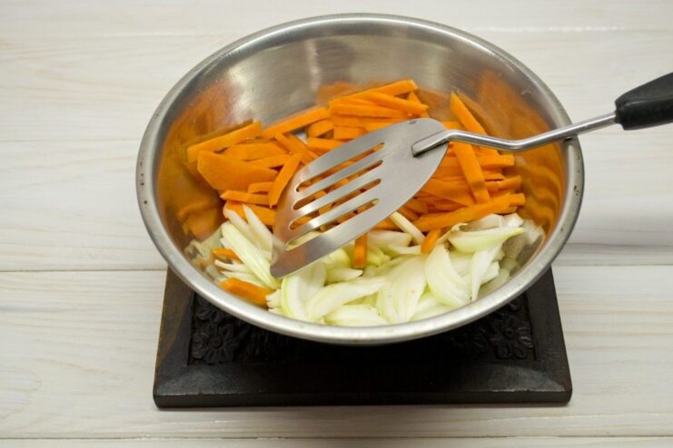 Sautéing onions and carrots to build the flavor base Sliced onions and carrots being sautéed in a pan.