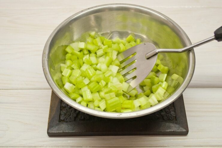Adding chopped celery to the sautéed vegetables Chopped celery being added to a pan with onions and carrots.