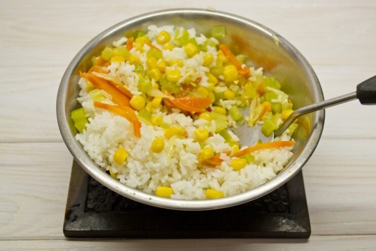 Combining the cooked rice with the stir-fried vegetables Cooked white rice being mixed with vegetables in a pan.