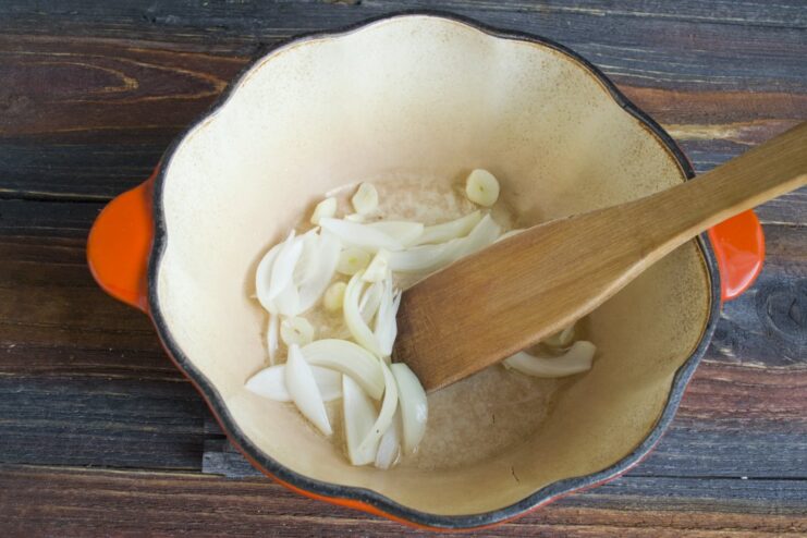 Step 1: Sautéing finely chopped onion and garlic until fragrant. Sliced onion and garlic being sautéed in oil in a black pan.