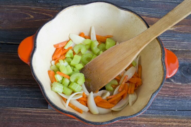 Step 2: Adding celery and carrots to build the flavor base. Chopped celery and julienned carrots being sautéed with onions in a pan.