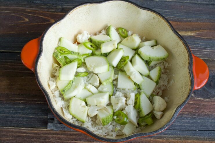 Step 4: Layering zucchini and chili on top of the rice. Diced zucchini and sliced green chili layered over rice and vegetables in a pan.