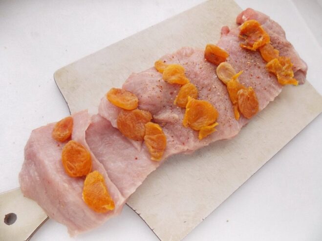 Adding the Sweet Dried Apricot Filling to the Pork Softened dried apricots arranged in rows over a seasoned, flattened piece of pork loin.