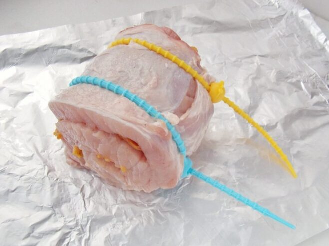 Securing the Pork Roll with Silicone Ties Securing the raw pork and apricot roll with red silicone kitchen ties.