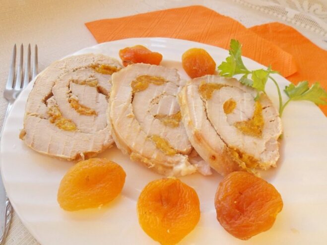 A platter of sliced pork roll with a vibrant dried apricot filling, garnished with fresh herbs.