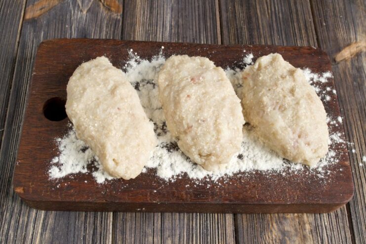 Shaping and Breading the Pollock Patties Before Frying Hands shaping a fish patty and coating it in flour on a wooden board.