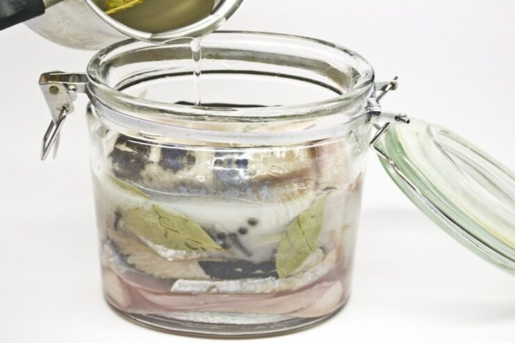 Step-by-step: How to prepare and brine herring at home for the perfect pickled fish. Glass jar filled with herring fillets and pickling brine, including spices like bay leaves and peppercorns.