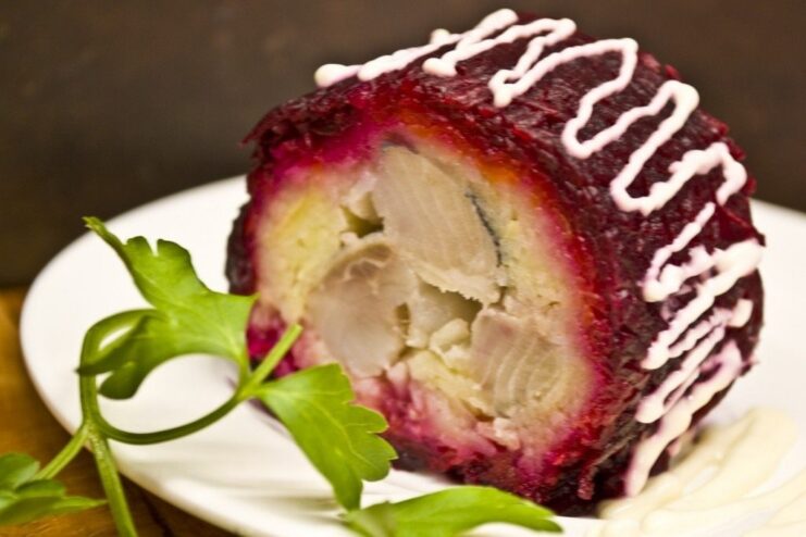 A close-up of a Shuba Salad Roll, sliced to show the vibrant layers, served on a plate.