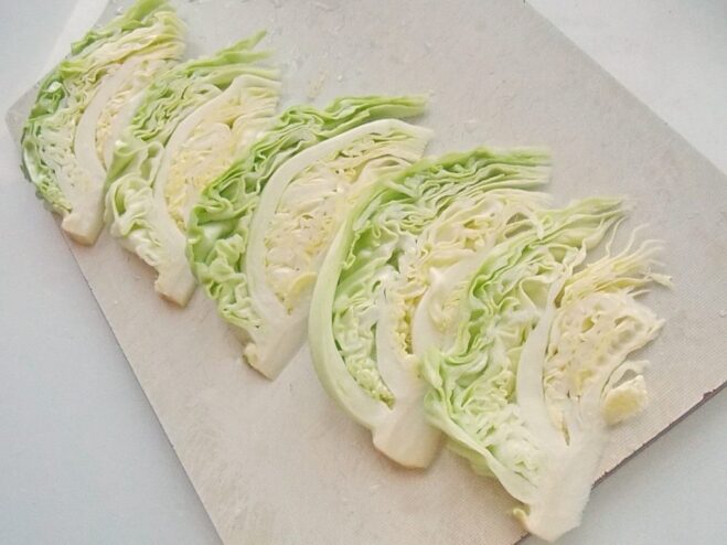 Slicing a head of young cabbage into wedges for the schnitzel recipe A head of young cabbage being cut into thick wedges on a cutting board.