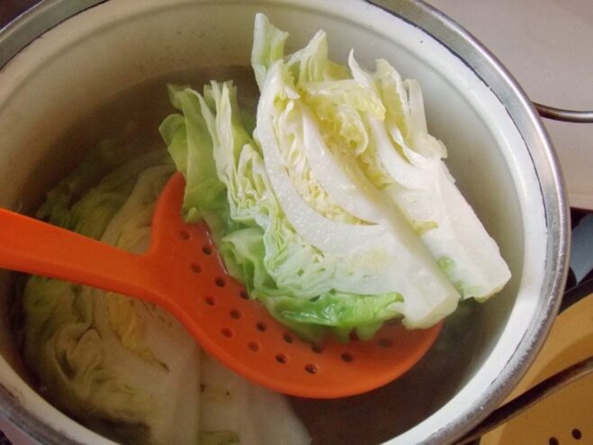 Using a skimmer to take boiled cabbage out of the pot A slotted spoon lifting a wedge of boiled cabbage from a pot.