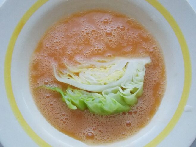 Dipping a cabbage wedge into a bowl of beaten eggs A wedge of cabbage being dipped into a bowl with whisked eggs.