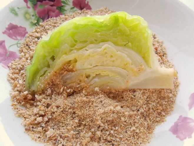 Coating the egg-dipped cabbage wedge in breadcrumbs A cabbage wedge being thoroughly coated in a plate of breadcrumbs.