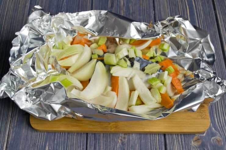 Adding Aromatic Vegetables to the Mackerel Fillet Chopped carrots, onions, and celery being placed on top of mackerel fillets.