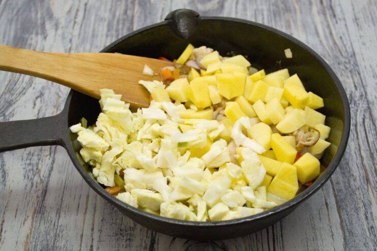 Adding Hearty Vegetables: Potatoes and Cabbage Diced potatoes and shredded cabbage being added to the pan with chicken and other vegetables.
