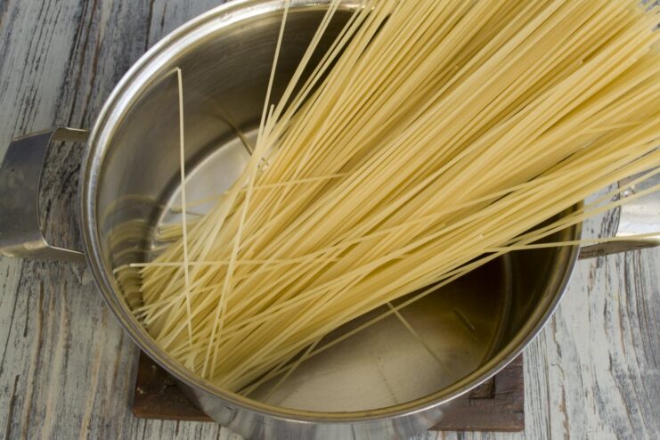 Cooking the spaghetti pasta until al dente Dry spaghetti being placed into a large pot of boiling water.