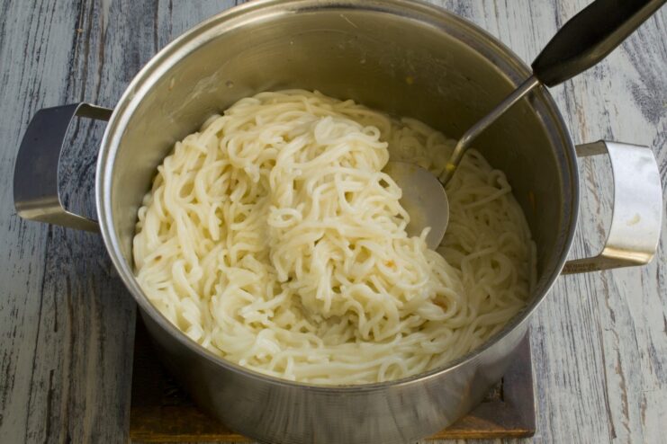 Draining the cooked spaghetti while reserving some pasta water Cooked spaghetti being drained in a metal colander over a sink.
