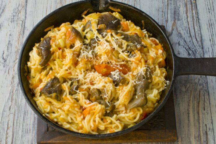 Final touch: serving spaghetti with a sprinkle of grated cheese A serving of spaghetti with mushrooms in a white bowl, topped with grated cheese.