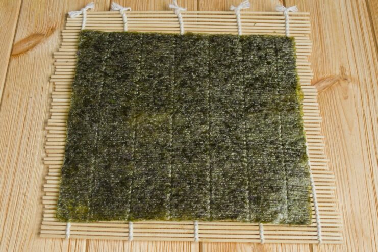 Starting the Sushi Roll: Placing Nori on a Bamboo Mat A bamboo sushi mat with a dark green nori sheet placed on top, shiny side down.
