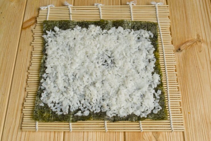How to Properly Spread Sushi Rice on a Nori Sheet Hands spreading a thin, even layer of cooked sushi rice over a nori sheet.