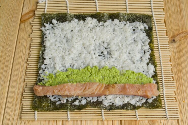 Adding a Kick: Spreading a Thin Line of Wasabi Paste A thin line of green wasabi paste being spread along the rice next to the fish.