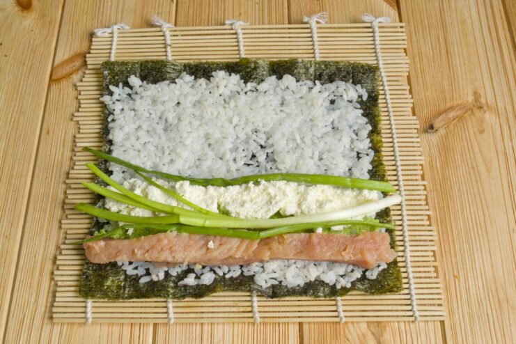 Adding Freshness: Placing Green Onions in the Sushi Roll Fresh green onion scallions being added to the other fillings for the maki roll.