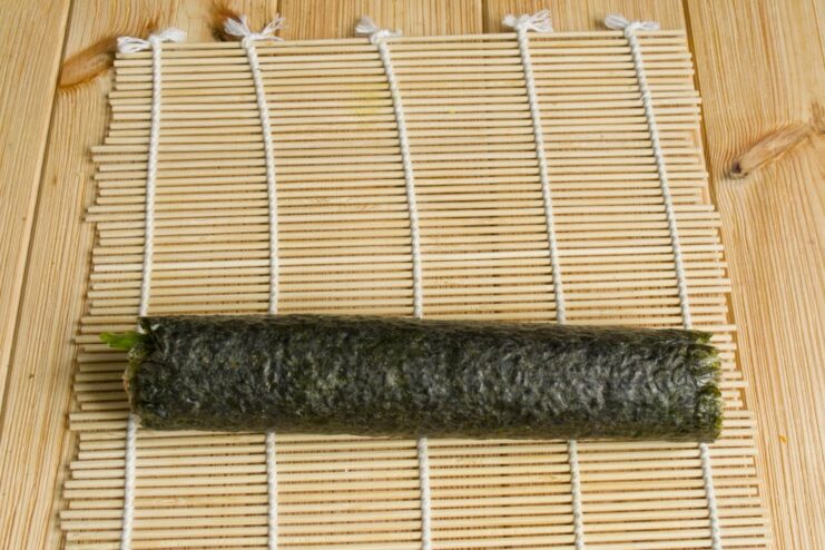 The Art of Rolling: Using a Bamboo Mat to Form a Tight Sushi Roll A bamboo mat being used to tightly roll the nori sheet with rice and fillings.