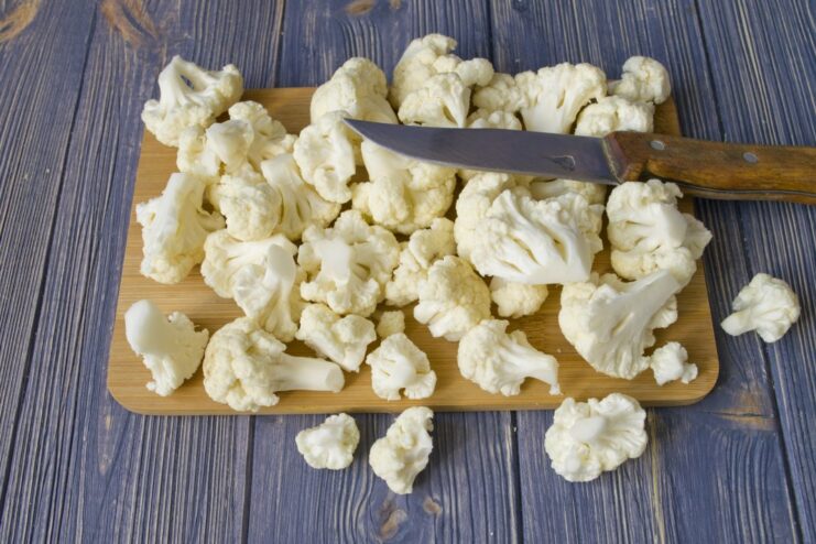 Preparing Cauliflower: How to Cut into Florets A head of cauliflower being broken down into smaller florets on a cutting board.