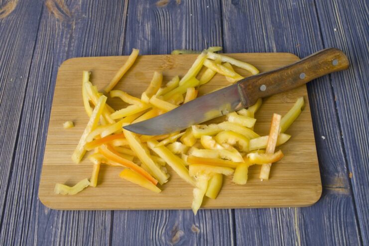 Slicing Bell Peppers for the Vegetable Stew A yellow bell pepper being thinly sliced on a cutting board.