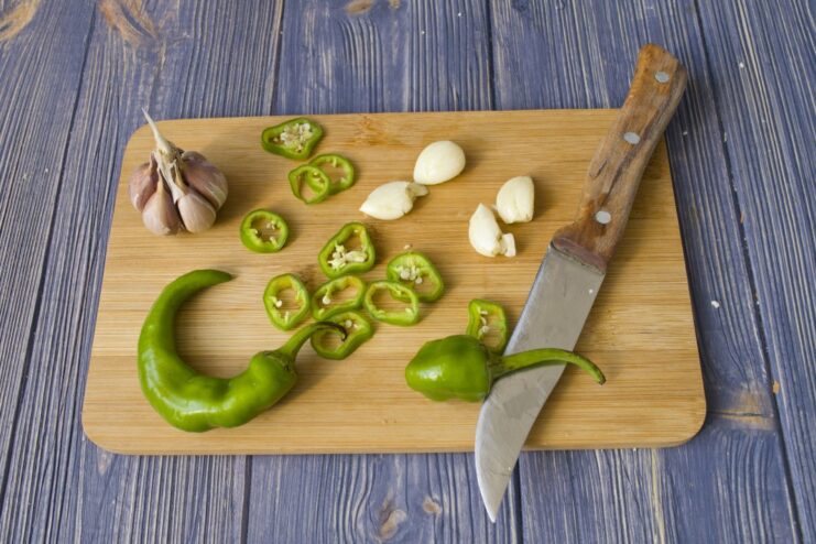 Prepping Aromatics: Slicing Garlic and Chili Sliced garlic cloves and chili pepper rings on a cutting board.