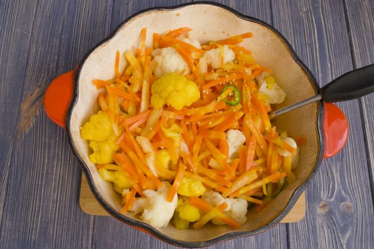 Combining Vegetables and Spices in the Pan A mix of vegetables including cauliflower, carrots, and peppers being cooked in a pan with spices.