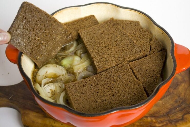 Using rye bread slices to create a unique, edible lid for the stew. Slices of dark rye bread arranged on top of chicken and onions in a pot.