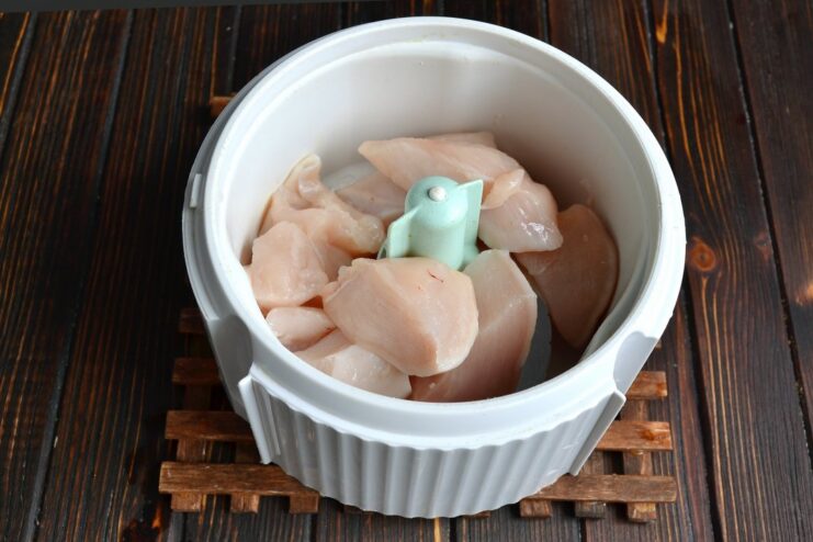 Chunks of raw chicken fillet inside a blender bowl, ready to be processed for meatballs.