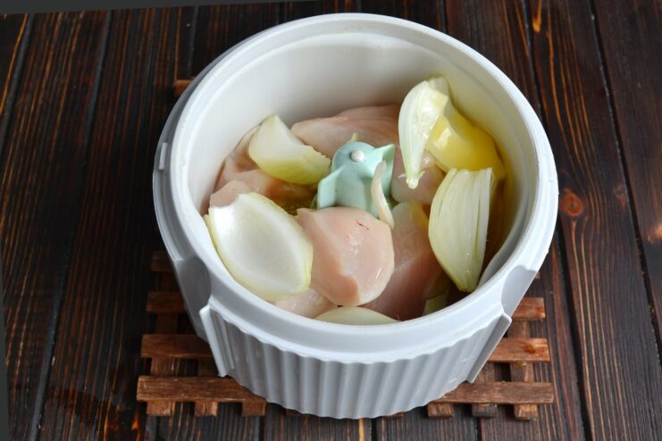 Chunks of chicken, coarsely chopped onion, and a cracked raw egg in a blender bowl.