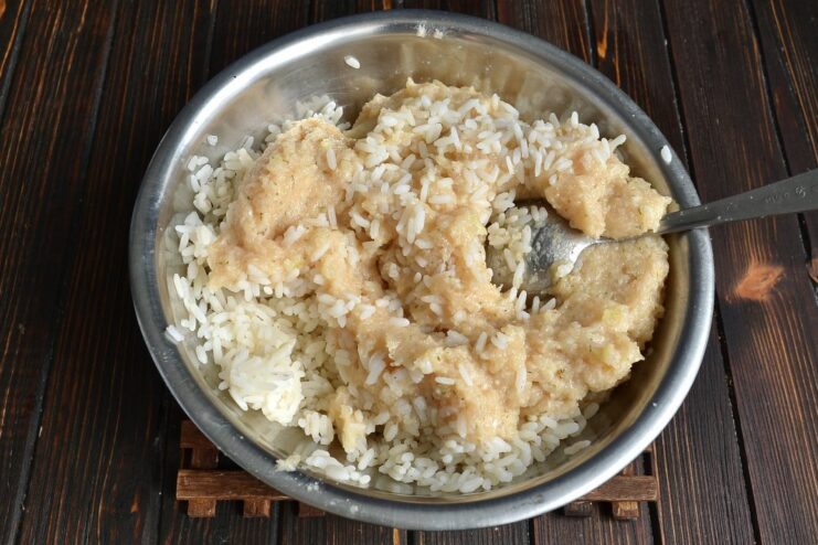 A glass bowl containing smooth ground chicken mixture being mixed with cooked white rice.