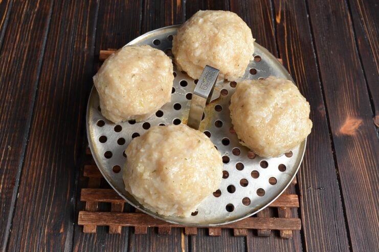 Raw, perfectly round chicken and rice meatballs arranged on a steamer rack, ready for cooking.