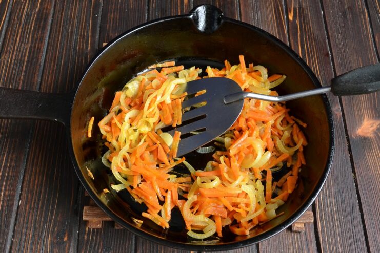 Finely chopped onions and grated carrots being sautéed in a frying pan until soft and golden.